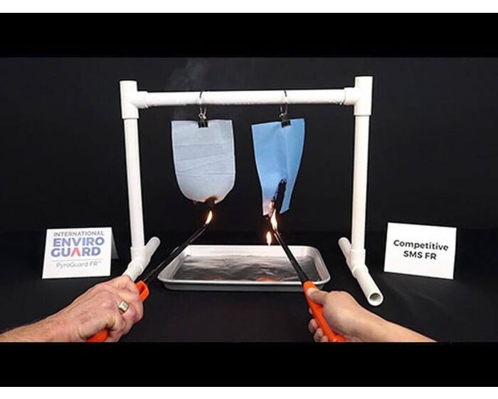Two hands holding lit matches approach two samples of material held in place by a white frame against a black background.